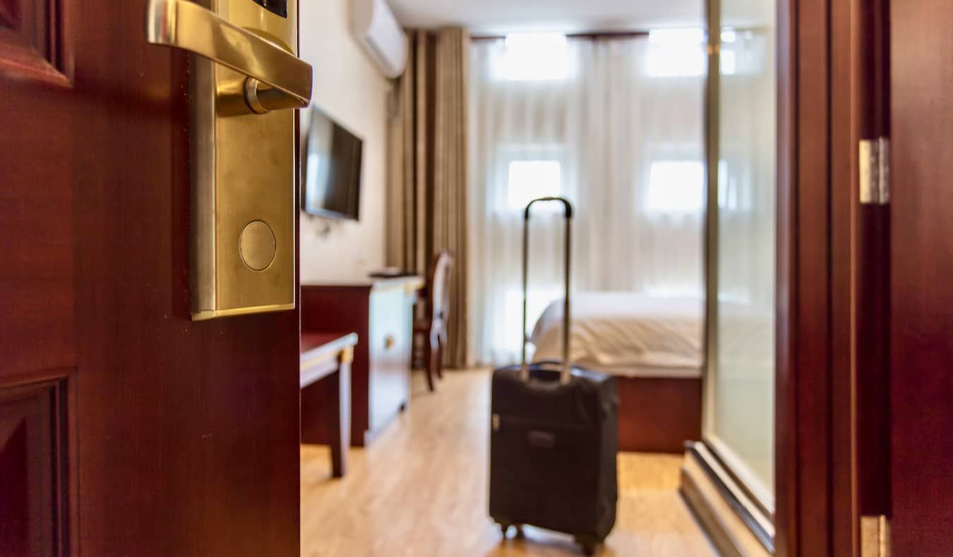 The door to a cozy hotel room opening, with a rolling suitcase nearby