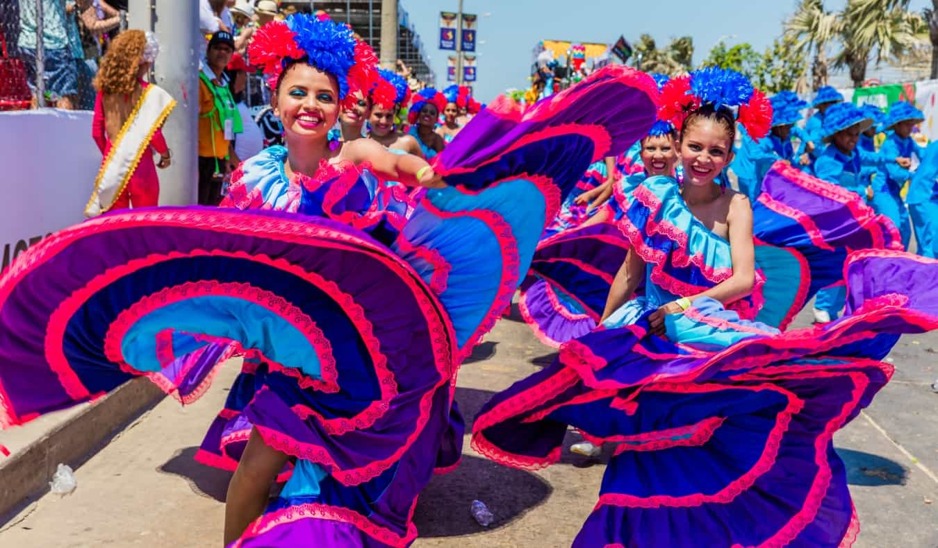 Women in bright pink and purple dresses, twirling around during Carnival in Barranquilla, Colombia