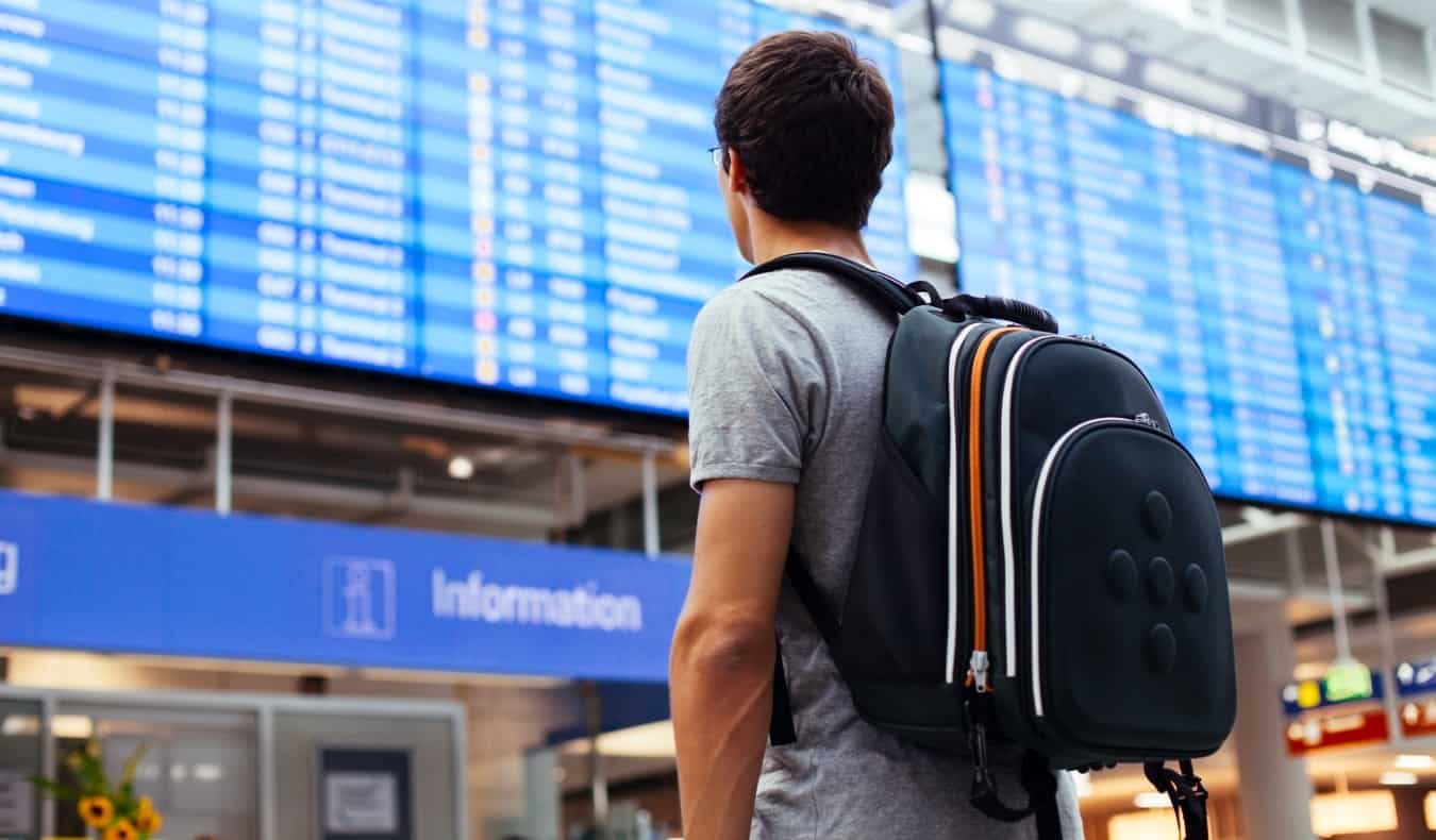 Jeune homme avec sac à dos à l'aéroport en regardant un horaire de vol