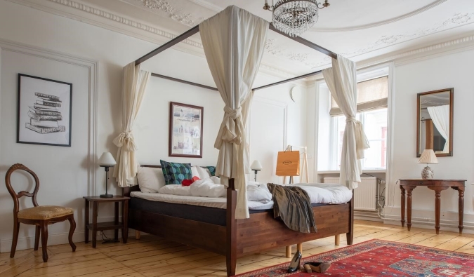 Wooden four poster bed in spacious guestroom with large windows, a chandelier, and hardwood floors at Castle House Inn in Stockholm, Sweden
