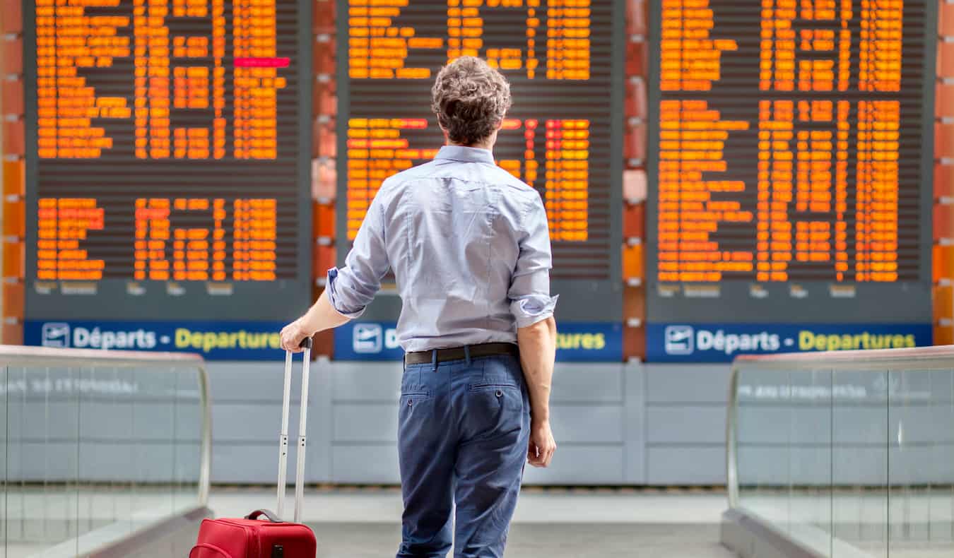 A man standing beside his luggage looking at an airport flight board
