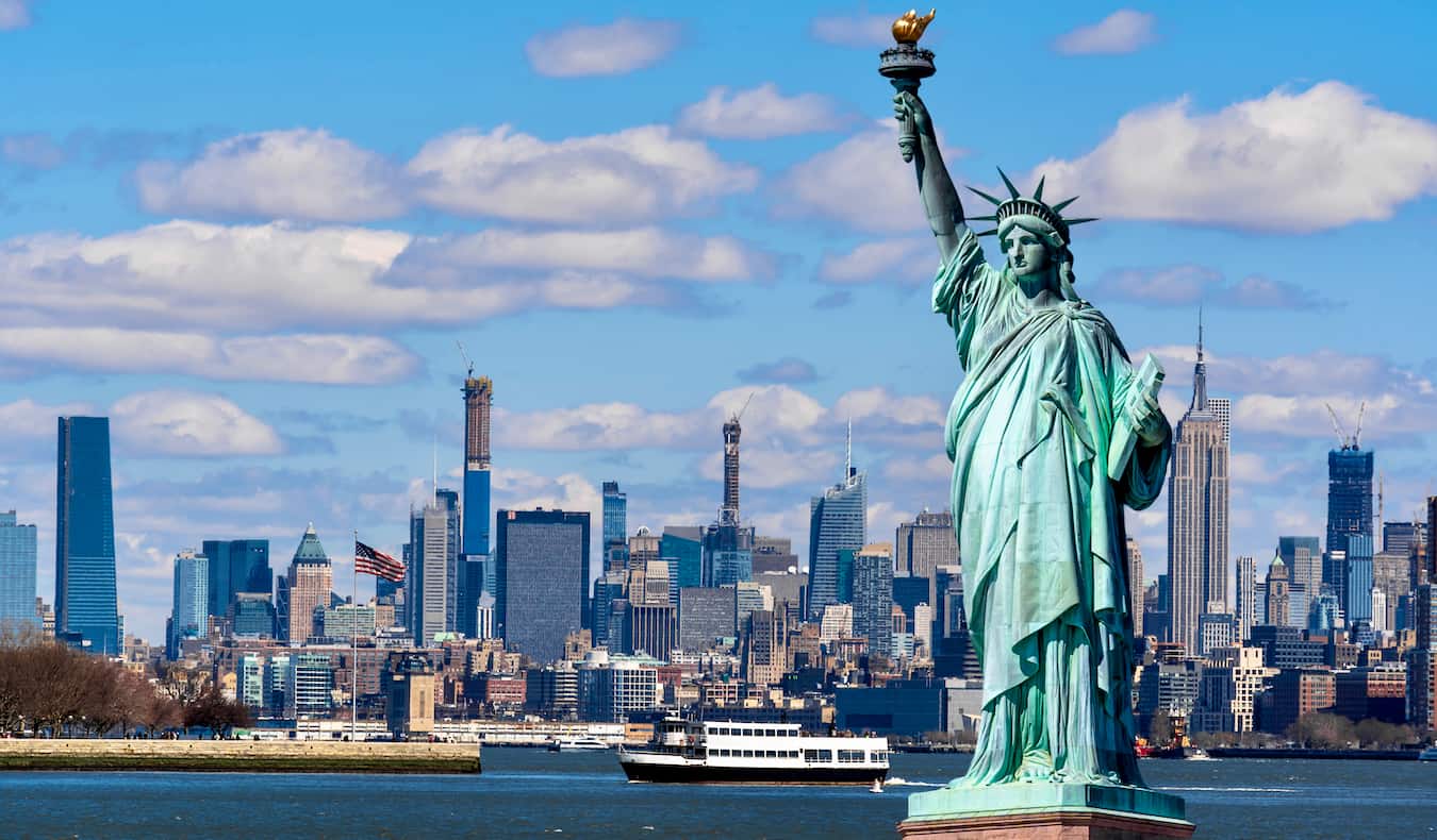 La icónica Estatua de la Libertad con NYC al fondo en un día soleado con cielos azules