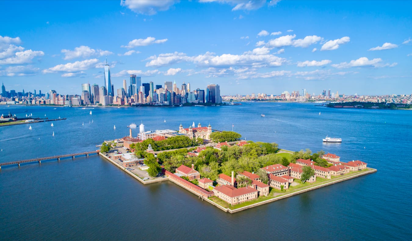 The famed Ellis Island as seen from above with NYC in the background on a sunny day with blue skies