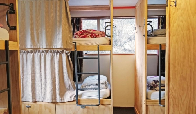 Wooden bunk beds with curtains at The Flaming Kiwi Backpackers in Queenstown, New Zealand.