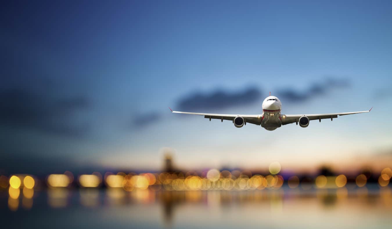 A huge commerical airliner flying through the dark blue sky as it comes in for a landing at an airport