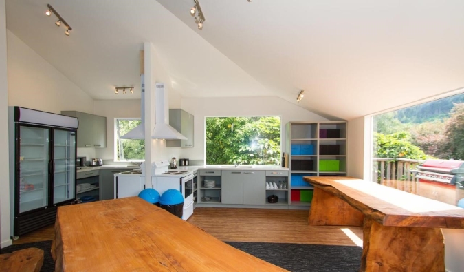 Expansive common area with long wooden tables, a kitchen area, and huge windows at Haka Lodge in Queenstown, New Zealand