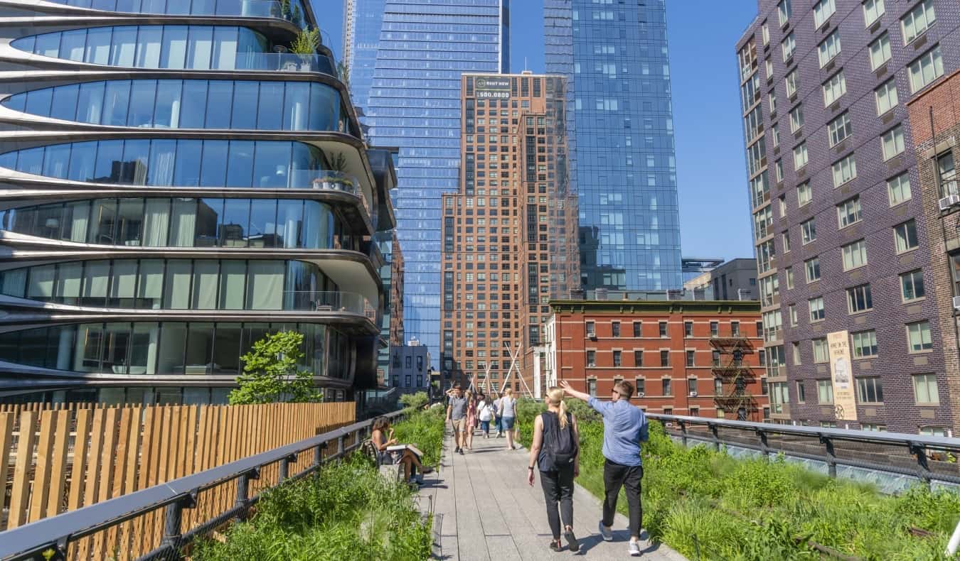 People walking on a pathway surrounded by greenery and tall skyscrapers on The High Line Park in the Meatpacking District in NYC
