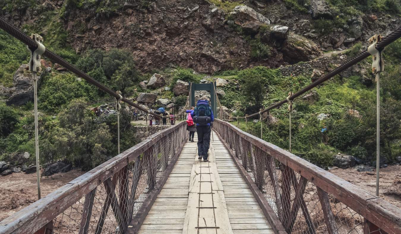A hiker on a wooden roped suspension bridge at the start of the Inca Trail in Peru