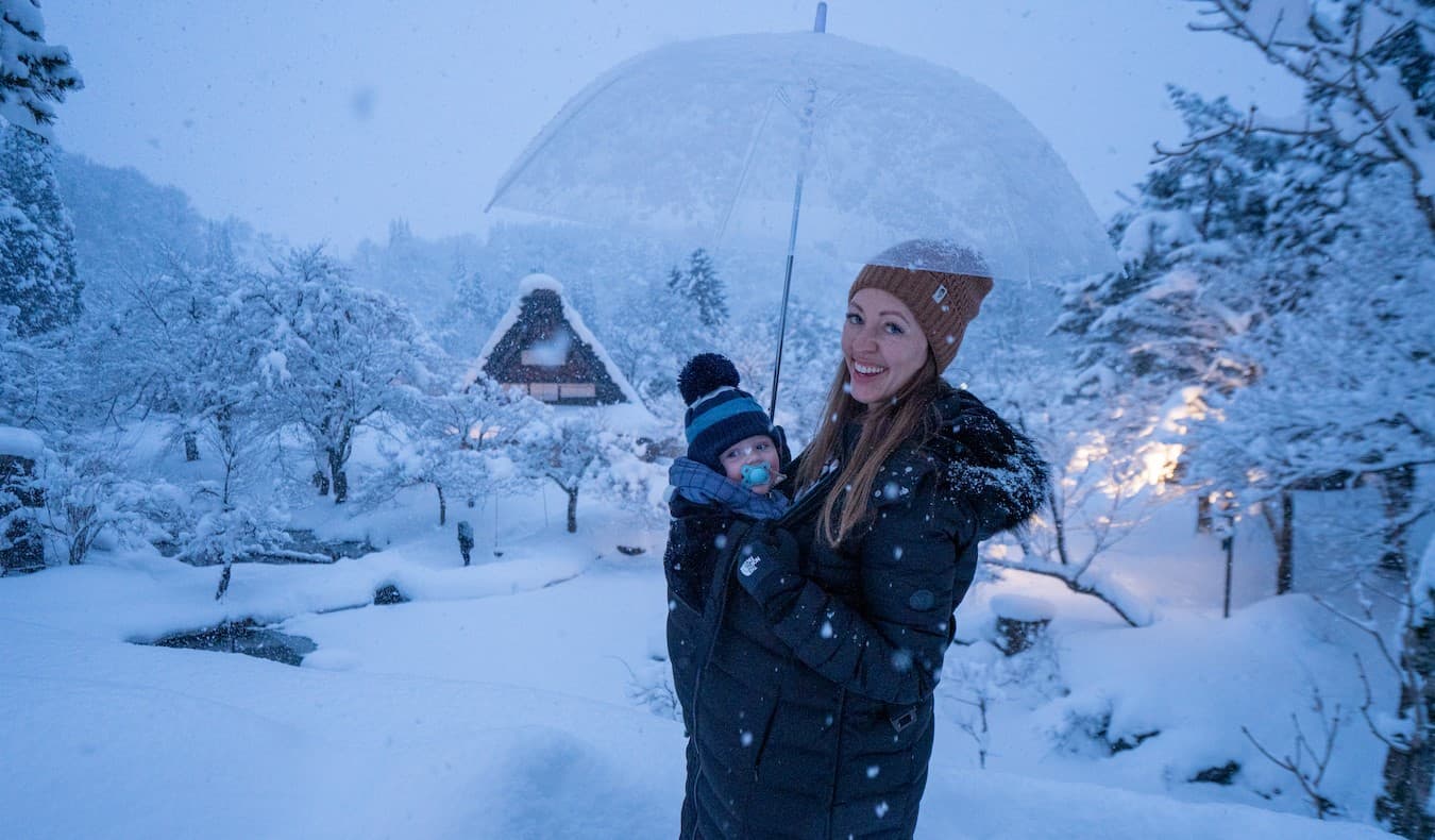 Blogger Kristin Addis of Be My Travel Muse with her infant son in a victual carrier as they stand in a snowy landscape in Japan