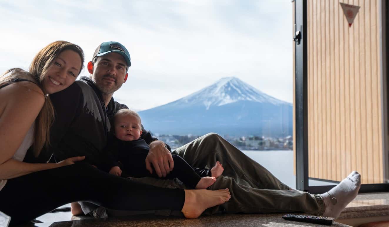 Blogger Kristin Addis of Be My Travel Muse with her partner and baby sitting next to a window in Japan with a snow-topped mountain in the background