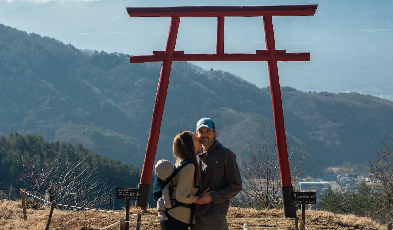 Blogger Kristin Addis of Be My Travel Muse with her partner and baby under a torii arch in Japan