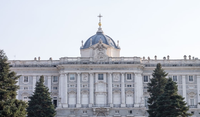 The stone facade of the Royal Palace, with pine trees in front, in Madrid, Spain