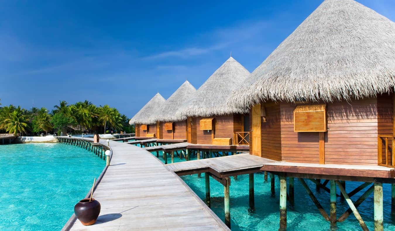 Thatched huts leading to a boardwalk over crystal clear waters in the Maldives