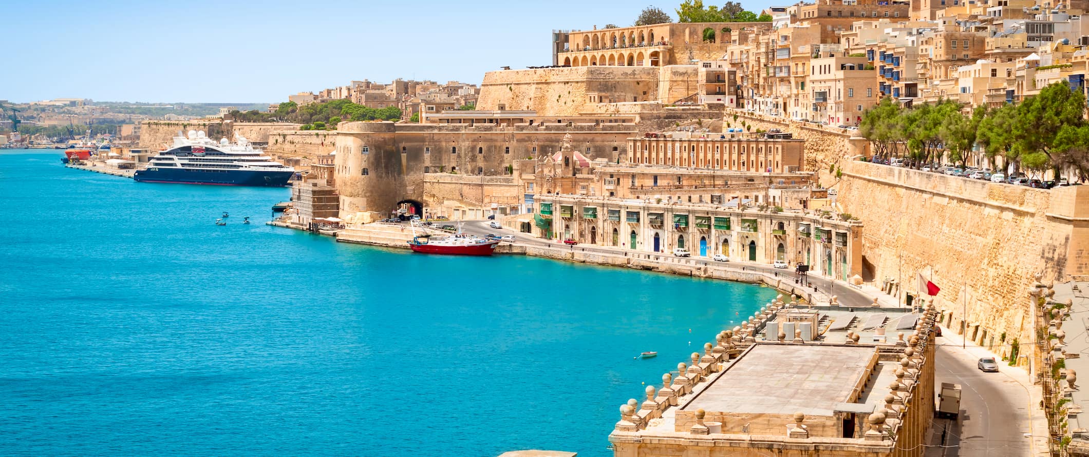 a view of the coast in Malta, lined by towering historic buildings near the harbor