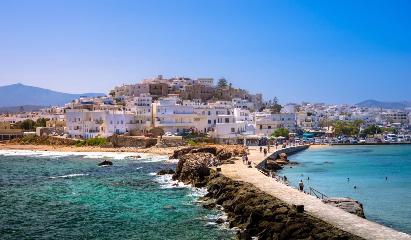 People walking down a stone causeway leading to the white-washed Old Town town in Naxos, Greece