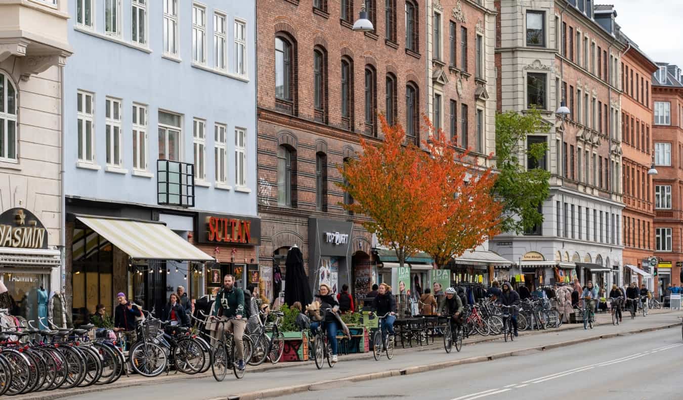 People biking down a street lined with restaurants in the neighborhood of Nørrebro in Copenhagen, Denmark