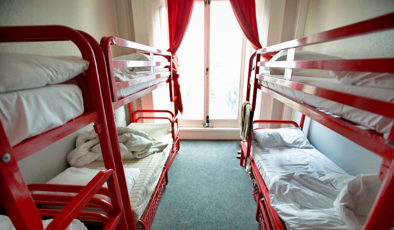 An empty hostel dorm with a pair of red bunk beds against the walls