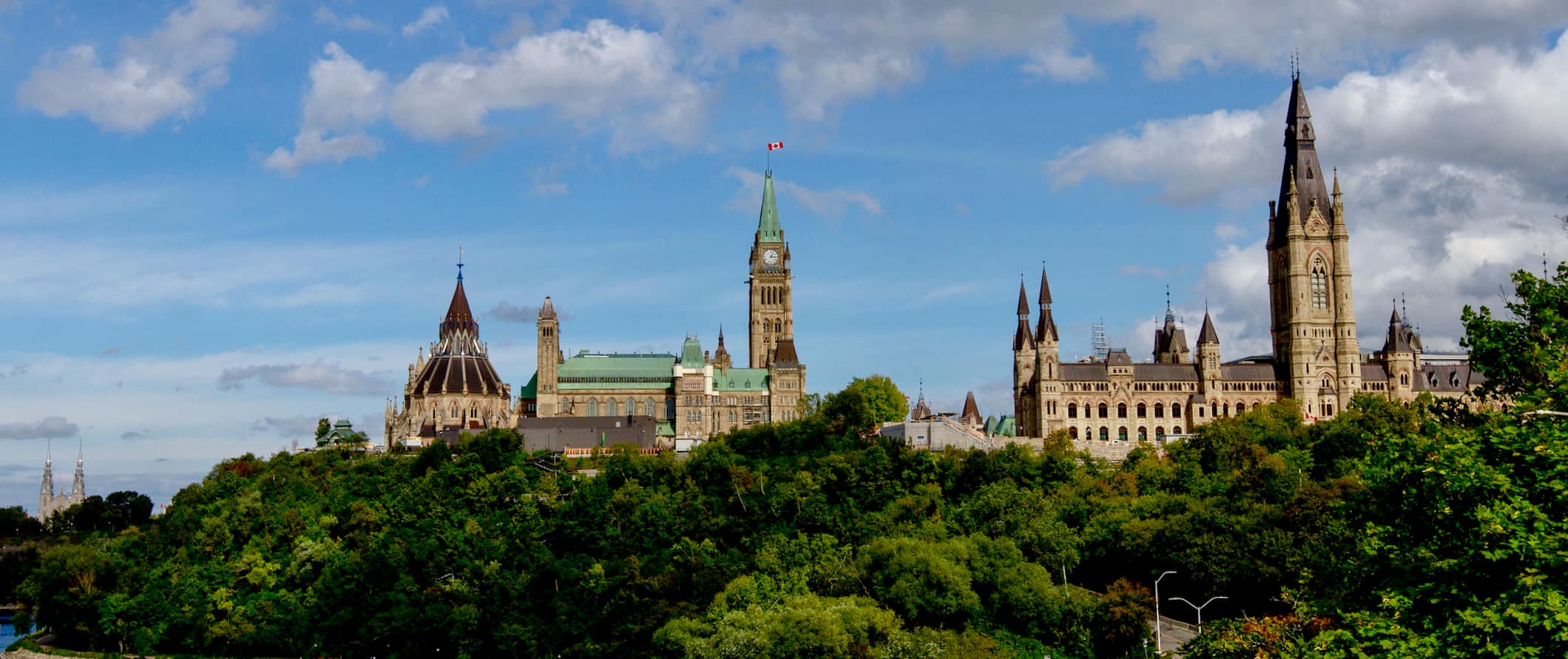 A view over the skyline of Ottawa, Canada, featuring the parliament buildings surrounded by lush green trees in summer