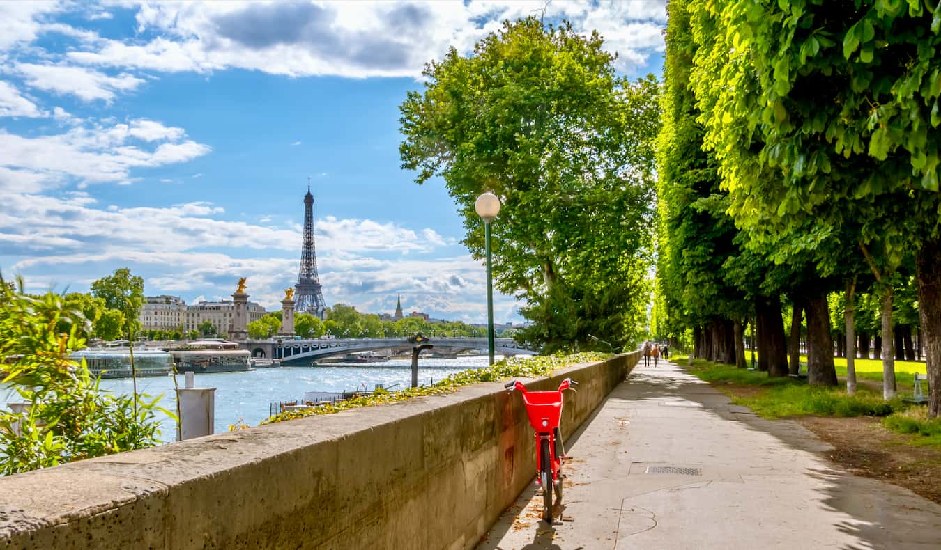 A red bike near the river in Paris, France with the Eiffel Tower in the distance