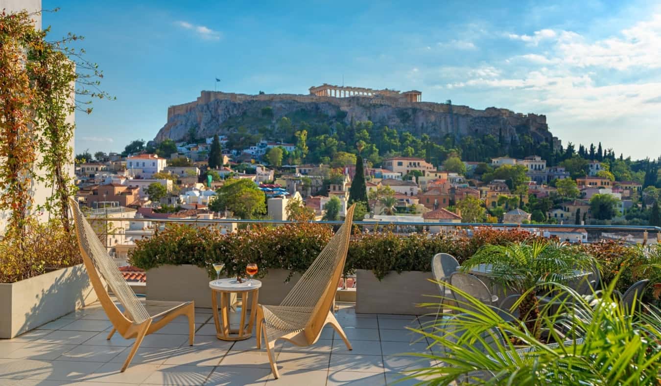 Wooden lounge chairs in front of a low table with champagne glass on it on the rooftop terrace of Plaka Hotel overlooking the Acropolis in Athens, Greece