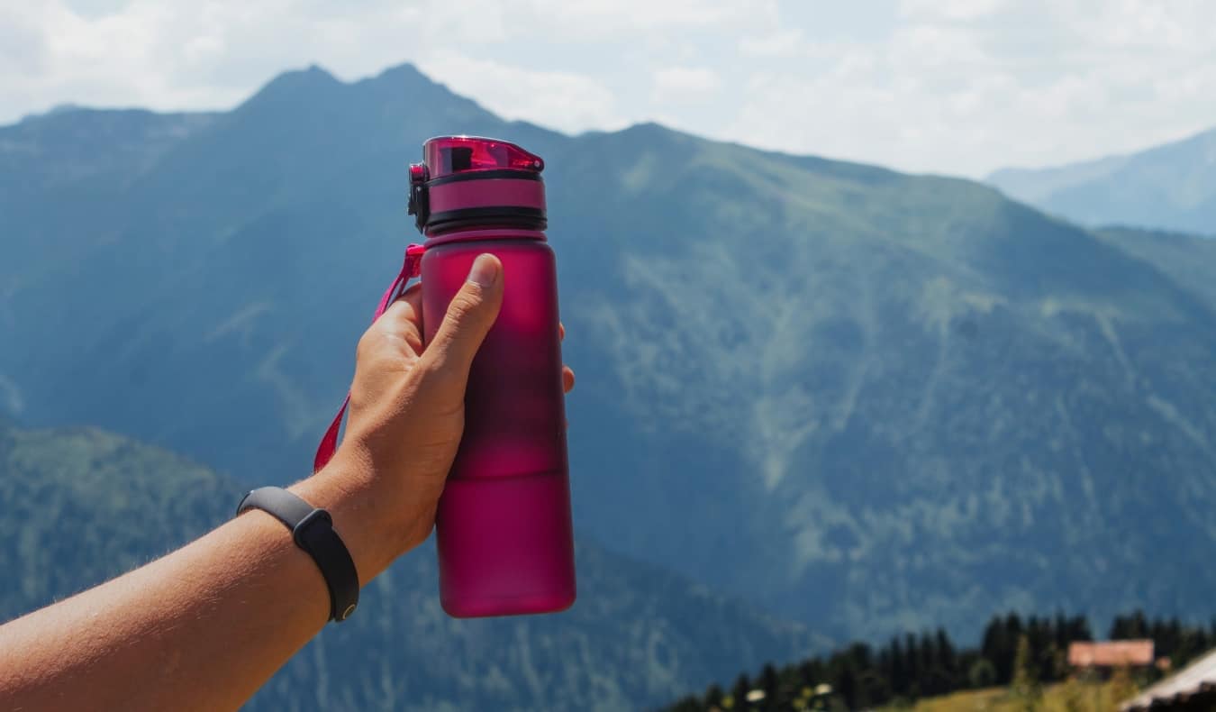 Person holding up a magenta reusable water against a mountainous backdrop