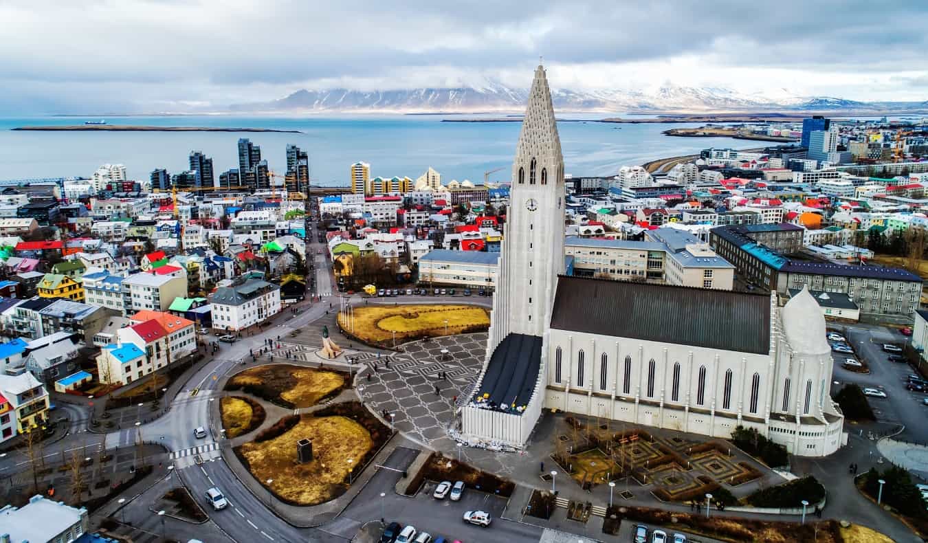 Aerial view of Reykjavik, Iceland with the beige Church of Iceland in its own plaza, towering over the low colorful buildings of the city