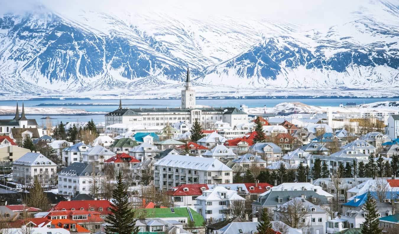 Reykjavik city skyline with colorful roofs, a church steeple, and snow-covered mountains in the background in Iceland