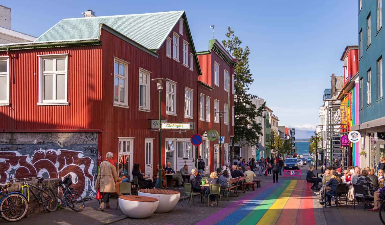 A streetscape in Reykjavik, Iceland, with people sitting in cafes along the rainbow-painted street