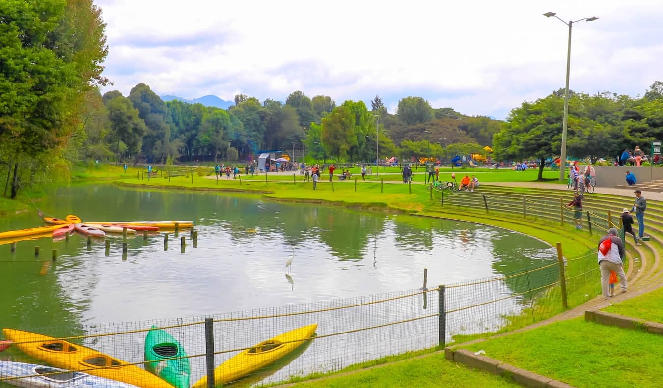 قوارب الكاياك تطفو في بحيرة ، ويحيط بها أشخاص يمشون ويركضون ، في حديقة سيمون بوليفار في بوغوتا ، كولومبيا