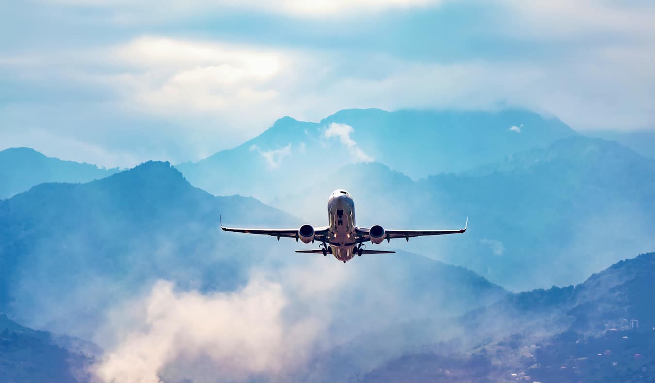 Un jet commercial solitaire décolle contre un ciel bleu vif et des montagnes lointaines
