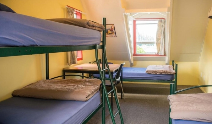 Simple metal bunk beds in a sunny yellow room at Southern Laughter Backpackers Hostel in Queenstown, New Zealand.