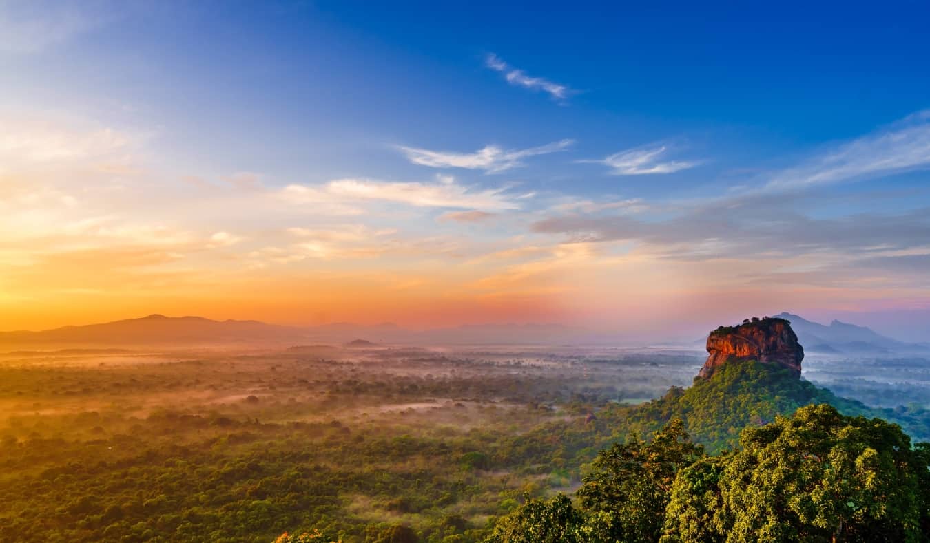Sunrise over an expansive lush landscape with Sigiriya rock, a large rock formation, rising above the trees in Sri Lanka