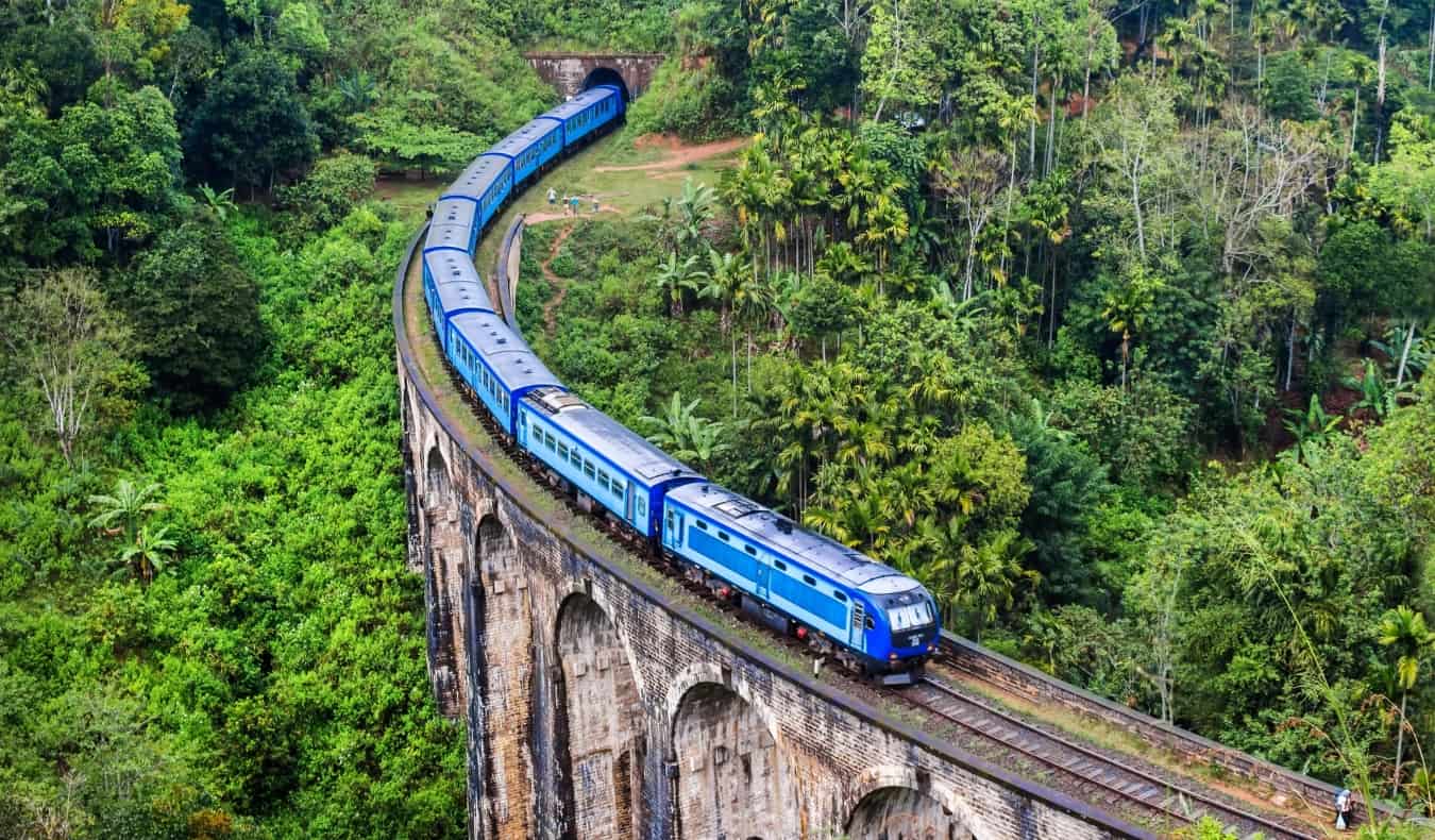 A blue train goes over the historic Nine Arch Bridge in Sri Lanka, surrounded by lush jungle