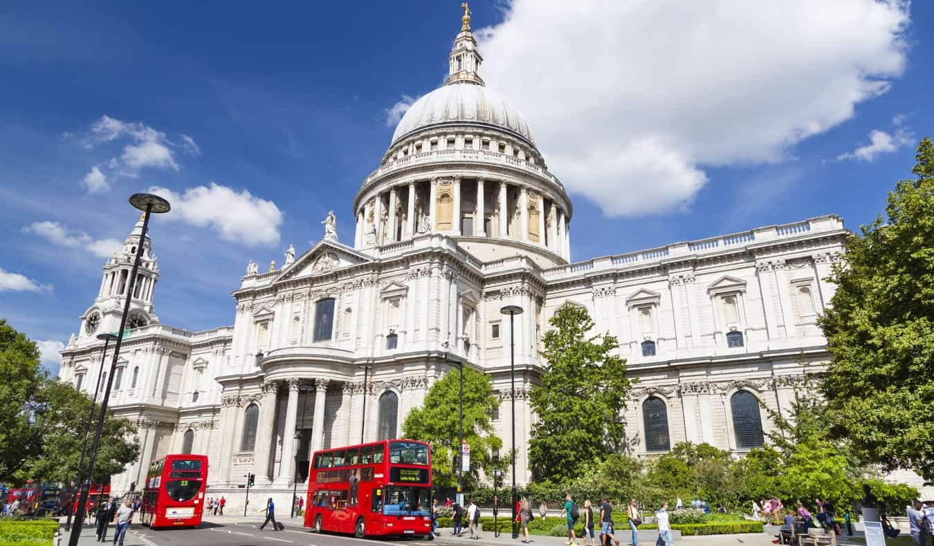Front view of the domed St. Paul's cathedral, with double decker red buses and people walking in front of it in London, England