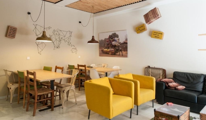 Eclectic worldwide zone of The Nomad Hostel with wooden tables and unexceptionable yellow lounge chairs in Sevilla, Spain