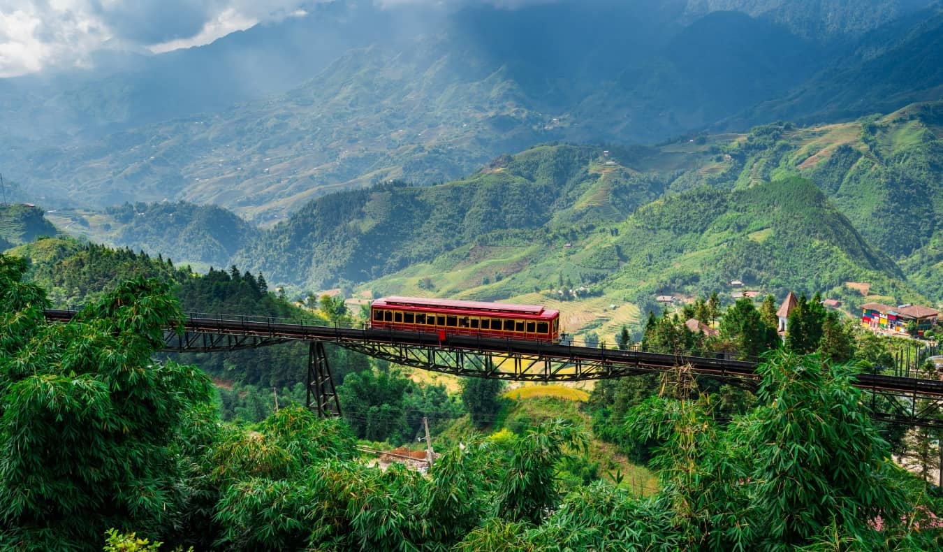 A beautiful, green, mountainous landscape with a train crossing on an elevated railway bridge in Vietnam