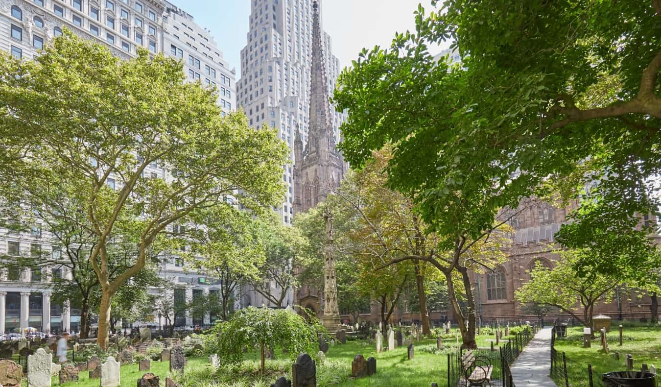 Old graves in a leafy graveyard surrounded by trees at Trinity Church in New York City, USA