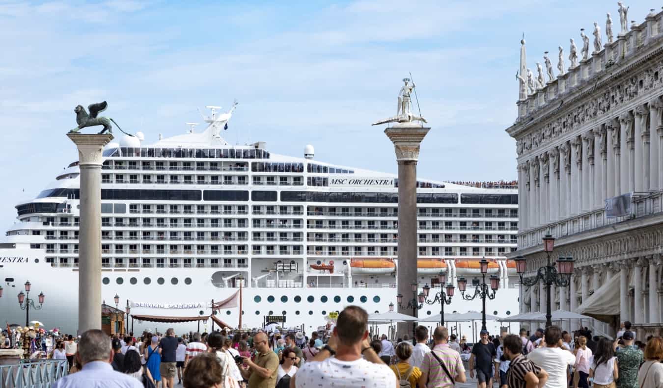 A cruise ship looms large over the historic square of Piazza San Marco in Venice, Italy, as crowds of tourists take photos in the foreground