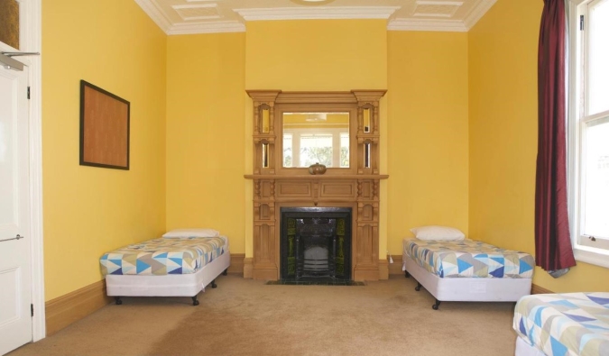Single beds on either side of a fireplace in a bright yellow room at Verandahs Parkside Lodge in Auckland, New Zealand