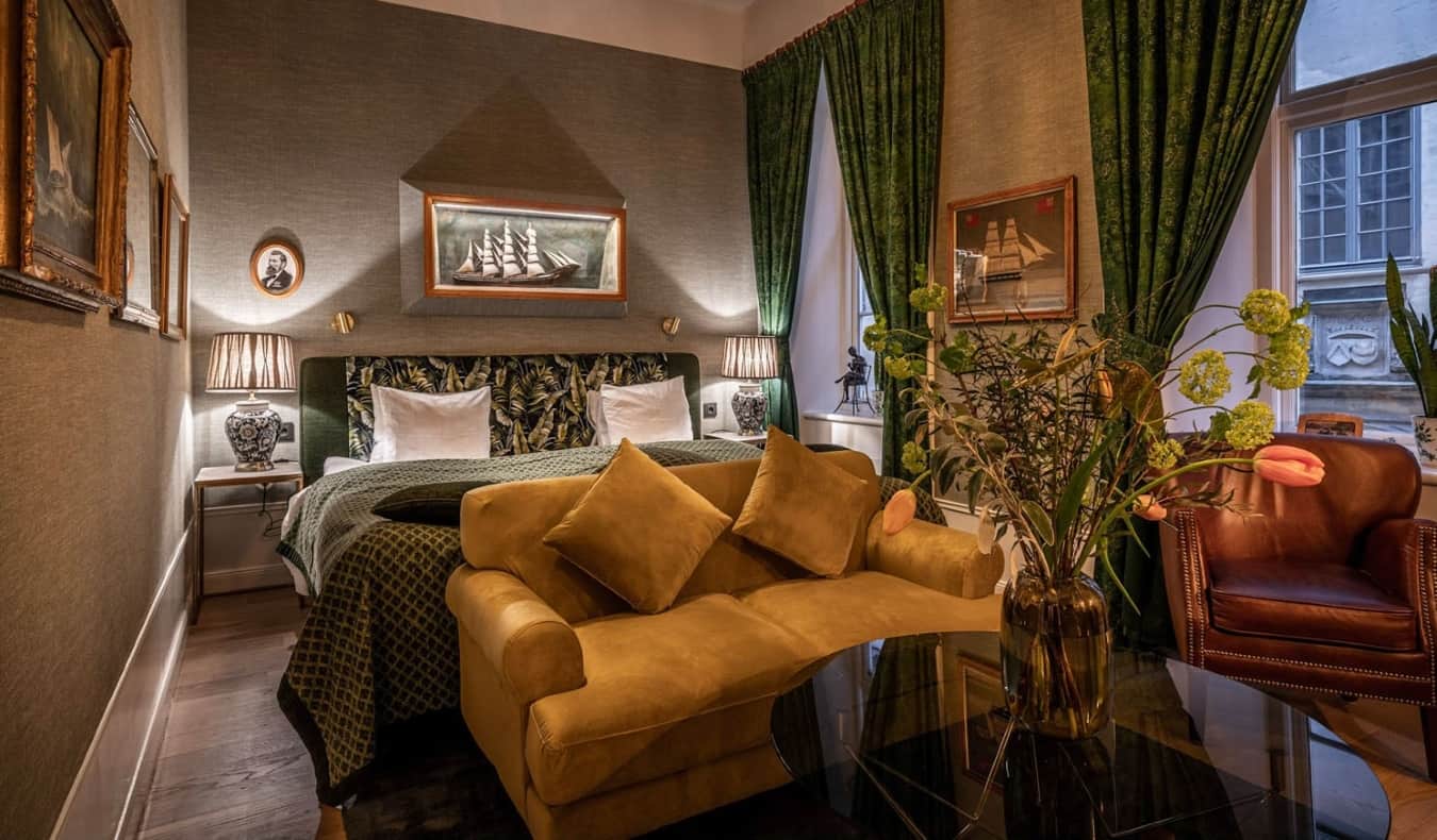 Luxurious guestroom with a velvet couch, leather easy chair, emerald drapes at the windows, and fabric-covered walls at Collectors Victory Hotel in Stockholm, Sweden