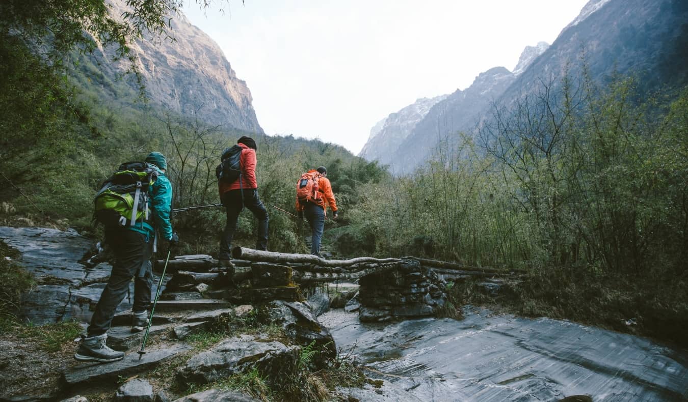 Group of trekkers cross a wooden bridge heading towards mountains in the Annapurna region of the Himalayas.