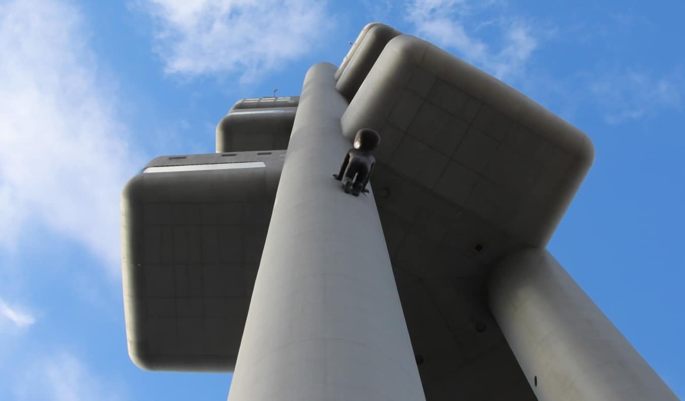 Looking up a pillar of the Zizkov TV Tower as large black sculpture baby climbs up it in Prague, Czech Republic