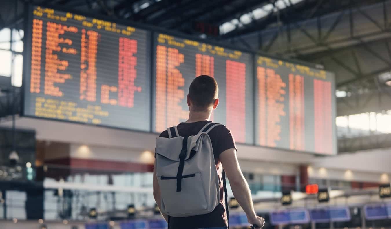 A man with a backpack on looks at an airport departures board full of red cancellations