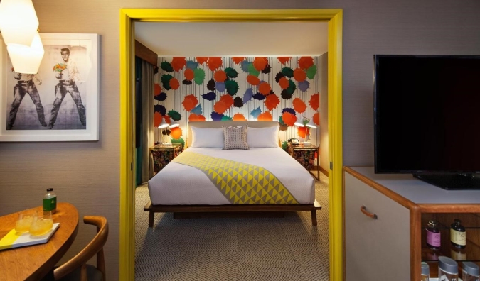 Um quarto de hotel iluminado com uma moldura de porta amarela e um mural colorido atrás da cama no The Kinney Hotel em Los Angeles