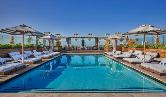 Une vaste piscine sur le toit entourée de parasols et de chaises longues à l'hôtel Sixty Beverly Hills à Los Angeles