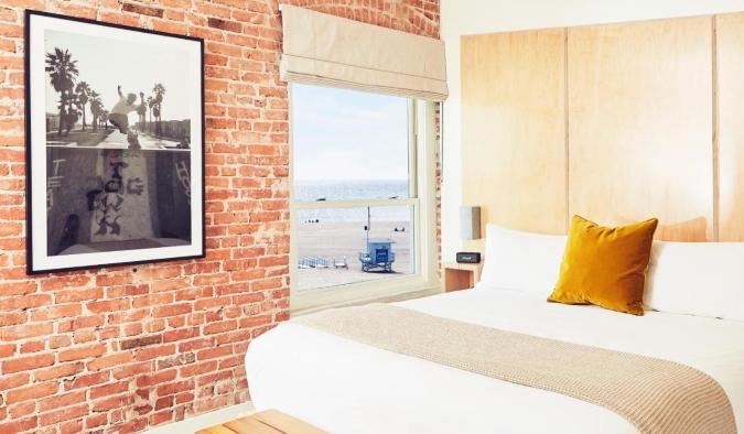 A king sized bed in a room with exposed brick walls overlooking the beach at Venice V hotel in LA