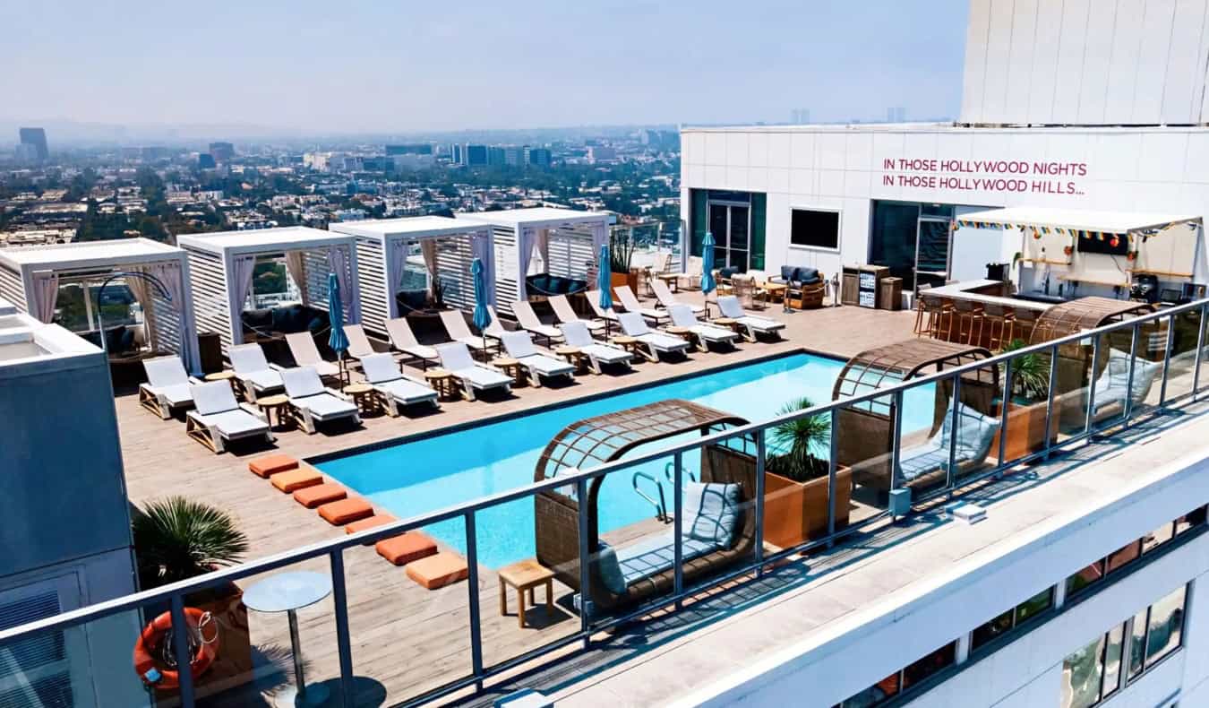 A piscina na cobertura cercada por espreguiçadeiras e cabanas no Andaz West Hollywood, um hotel cinco estrelas em Los Angeles, com o horizonte de Los Angeles ao fundo