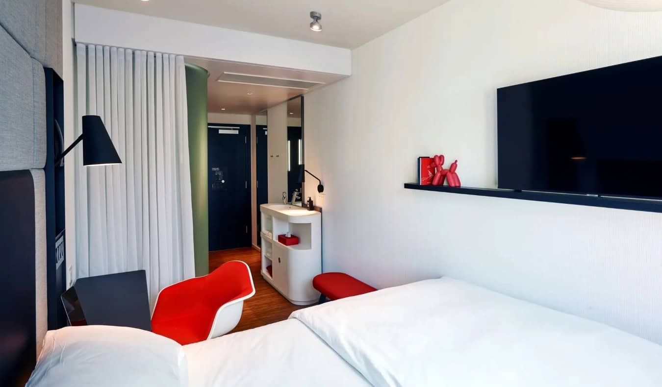 Um quarto de hotel compacto com uma cama, TV na parede e móveis vermelhos no hotel CitizenM Los Angeles