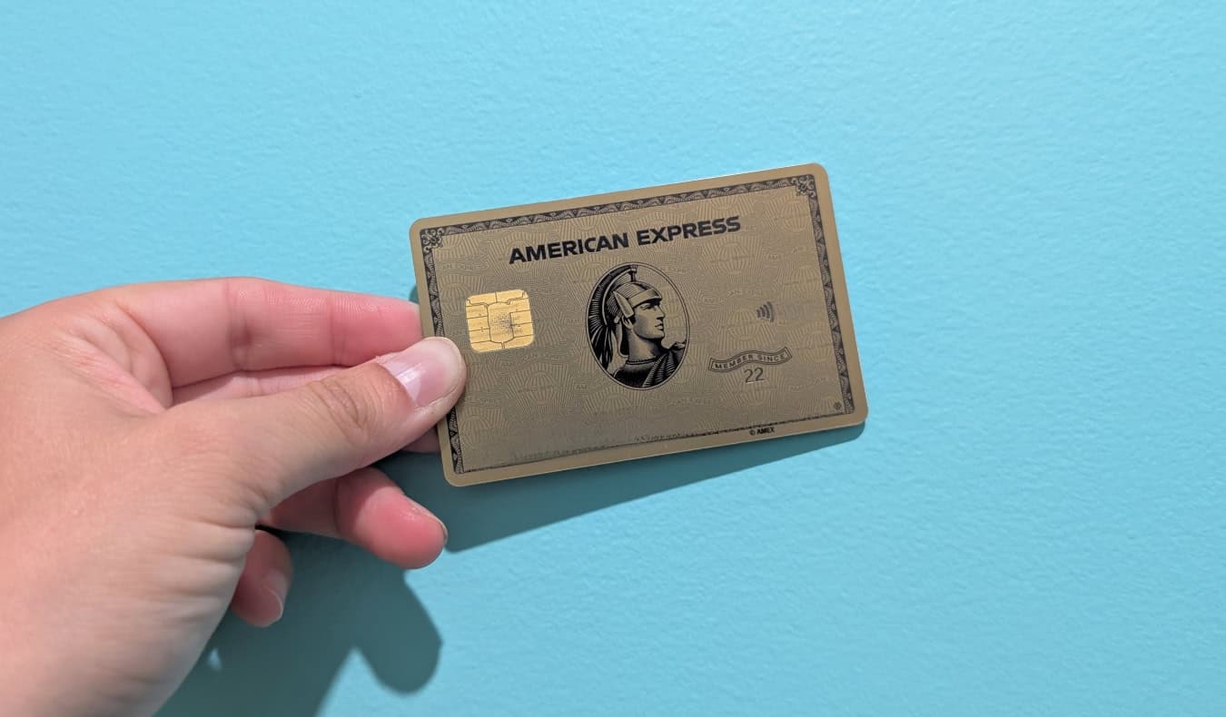 The American Express® Gold Card being held up in front of a bright blue wall