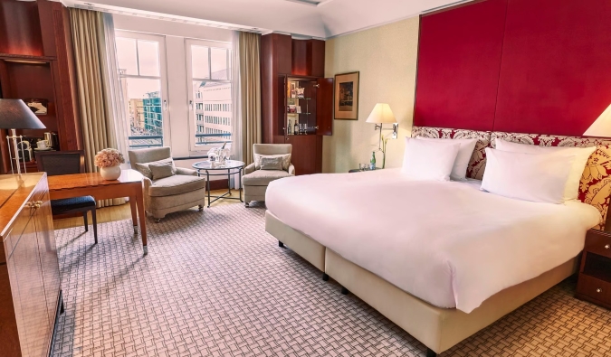 A stately guest room with carpeted floors, red fabric walls, a large window, and a desk at Hotel Adlon Kempinski Berlin, a five-star hotel in Berlin, Germany